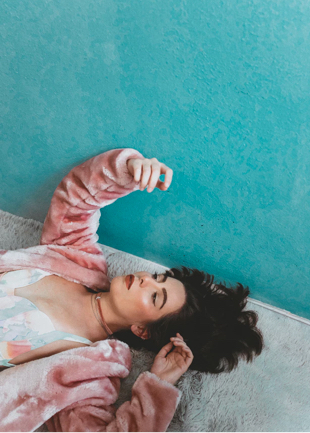Person wearing pink fuzzy sweater lying on grey carpet on teal floor.